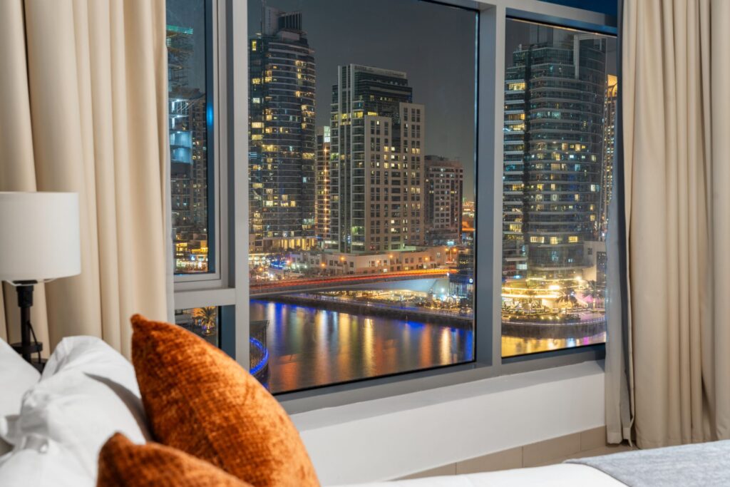 Bedroom window overlooking the Dubai Marina towers and canal at night