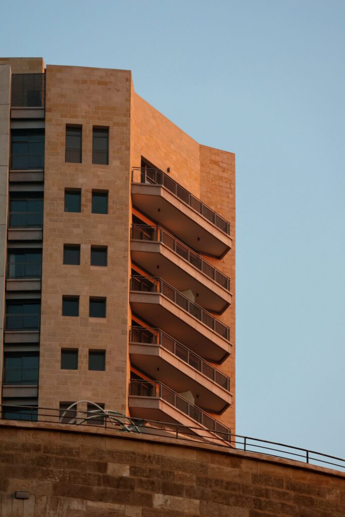 Warm sandstone high-rise facade with staggered cantilevered balconies at golden hour under a clear sky, representative of Canal Residence West Spanish Building in Dubai Sports City, Dubai