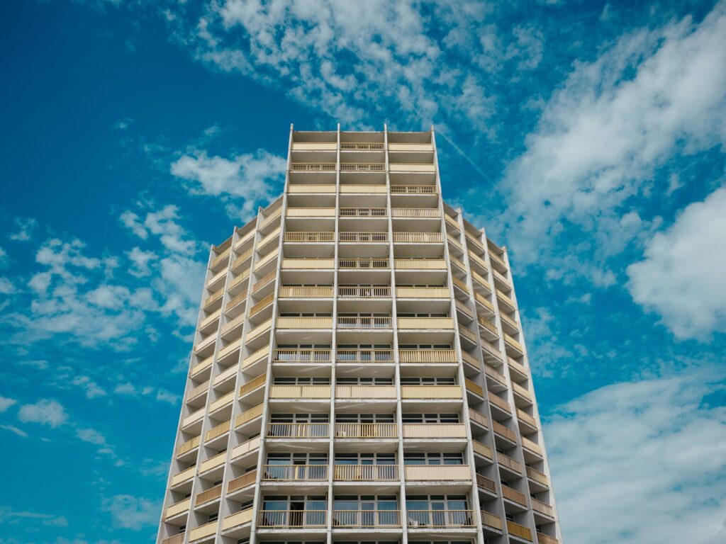Tall cream-colored high-rise apartment tower with rows of balconies against a clear blue sky in Dubai