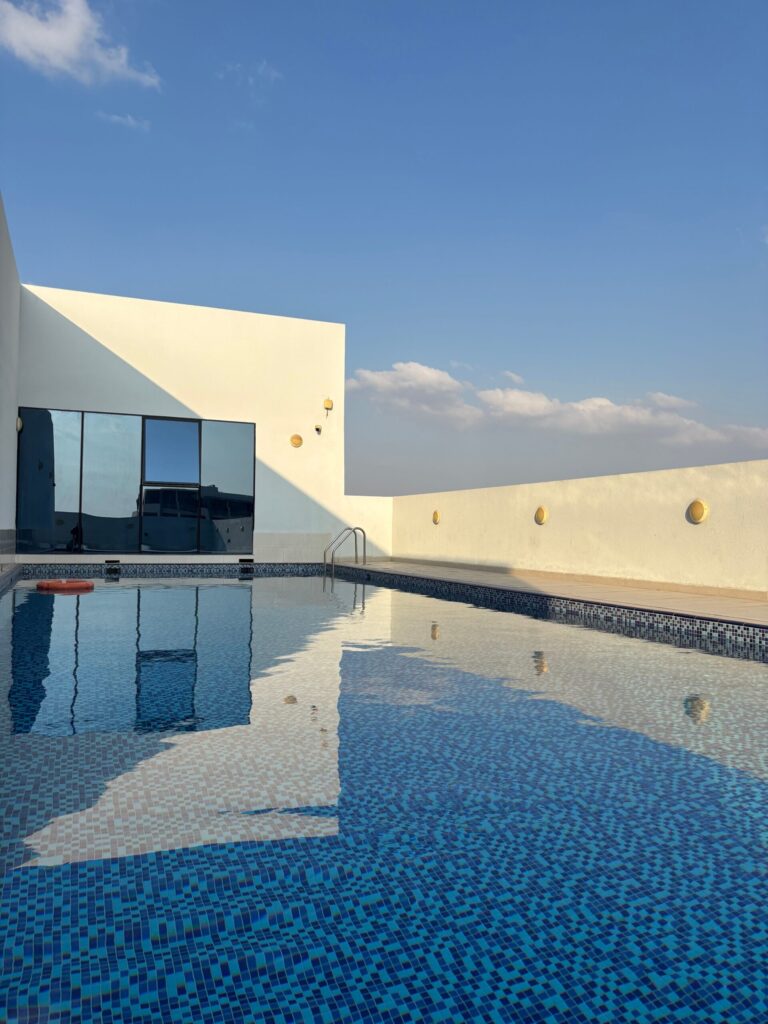 Clean rooftop swimming pool deck on a modern white residential building under a clear sky, representative of Golf Grove's private rooftop terrace amenity in Dubai Hills Estate