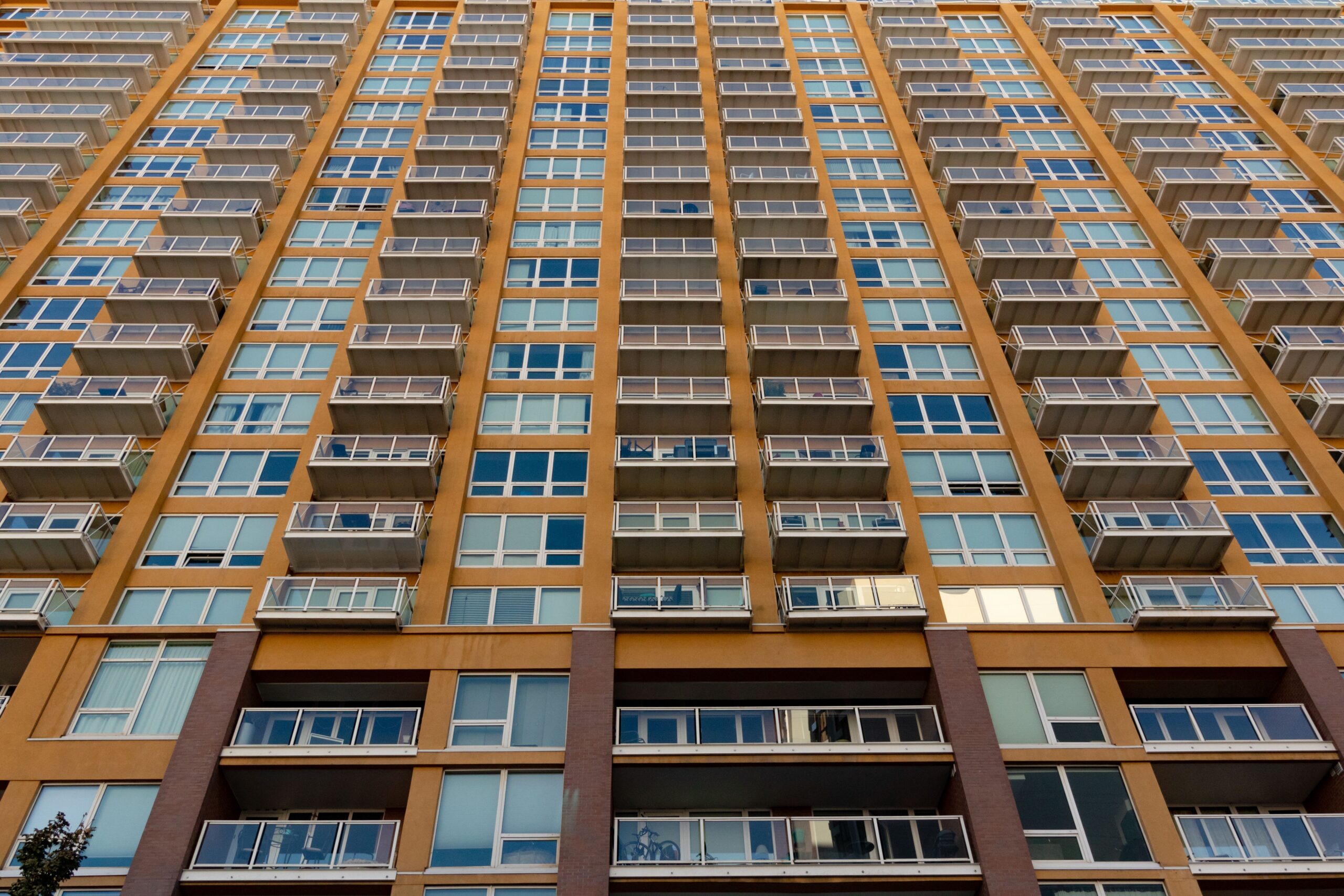 Low-angle view of a modern high-rise residential facade with rows of glass balconies in warm beige and gold tones, representative of Silicon Gates IV in Dubai Silicon Oasis, Dubai