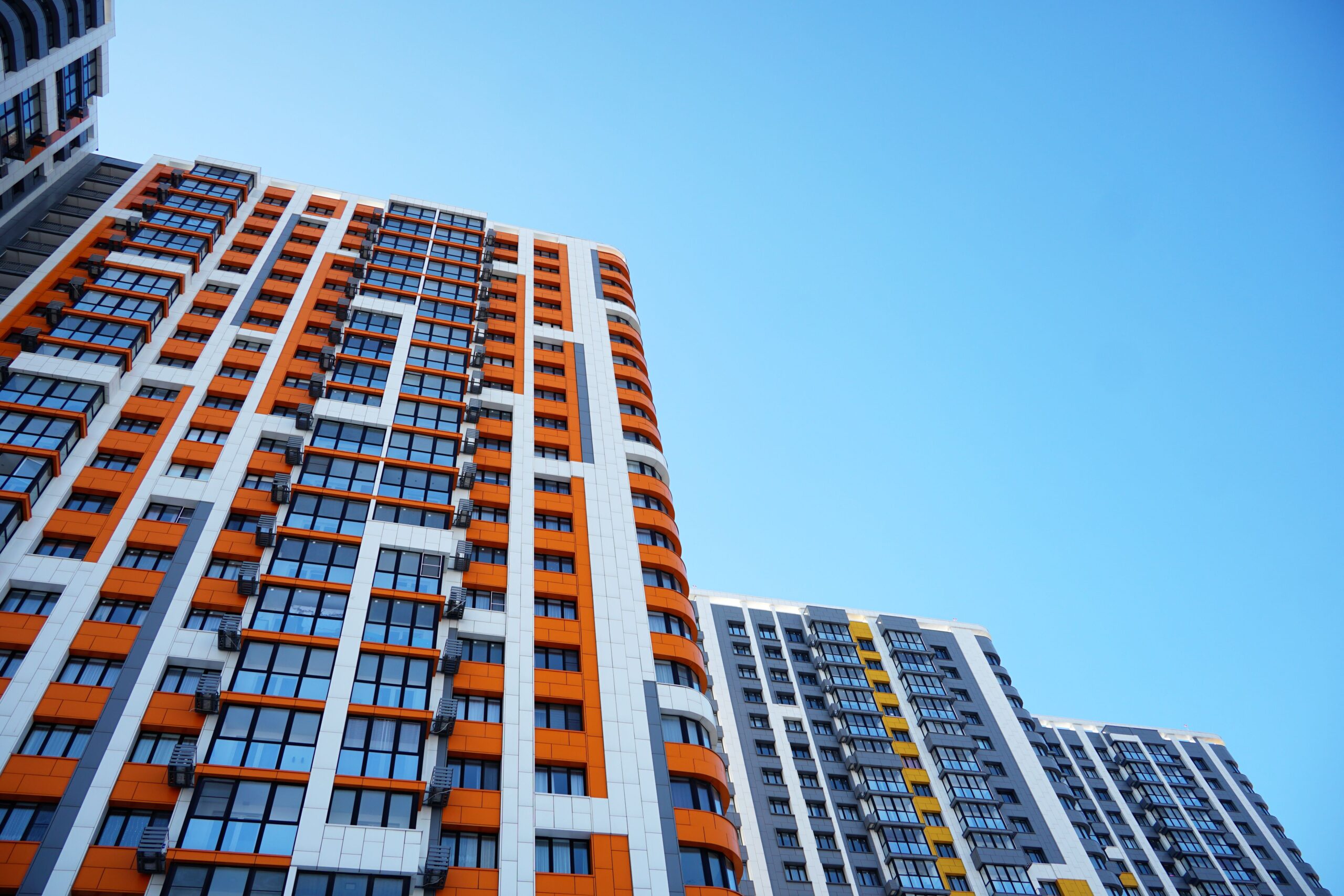 Upward view of a modern high-rise apartment building with bright orange and grey facade panels against a clear blue sky in Dubai