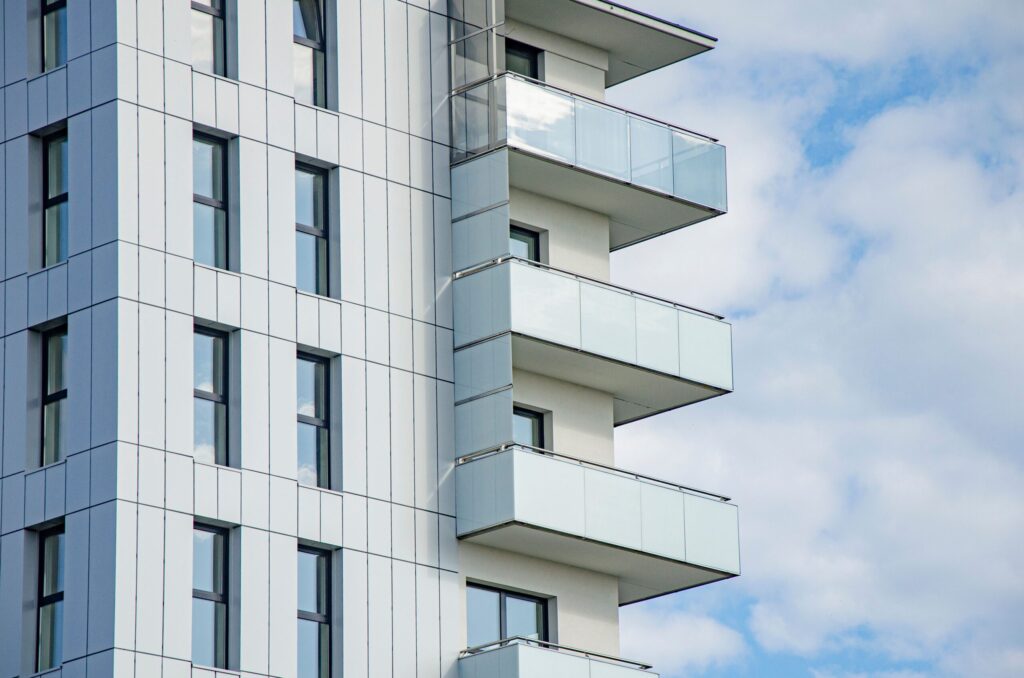 Modern high-rise apartment facade with glass-fronted balconies against a cloudy blue sky