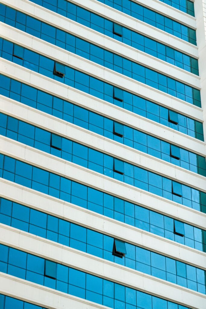 Close-up low-angle view of a modern Dubai residential tower with reflective blue glass windows and white banding, representative of Sondos Lily in DubaiLand Residence Complex, Dubai