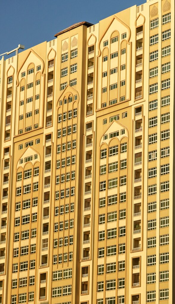 Tall golden-toned Dubai residential tower with Arabic-arch-inspired window surrounds, similar in style to Terhab Hotel & Towers, JVT