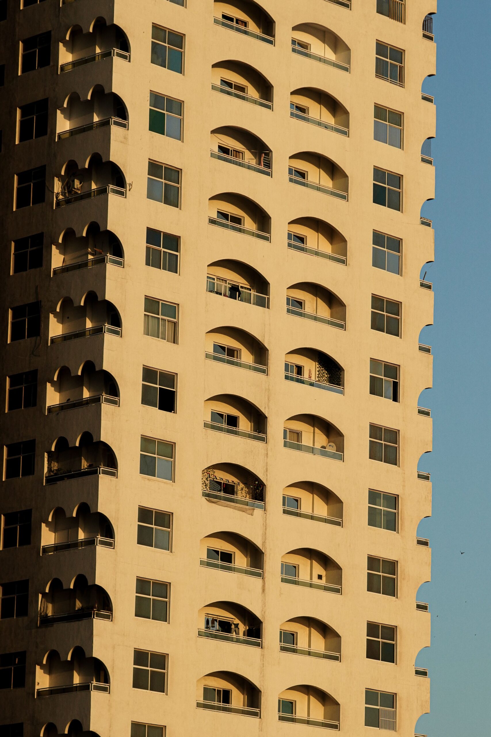 Low-angle view of a Dubai high-rise residential tower with distinctive arched balconies against a clear sky