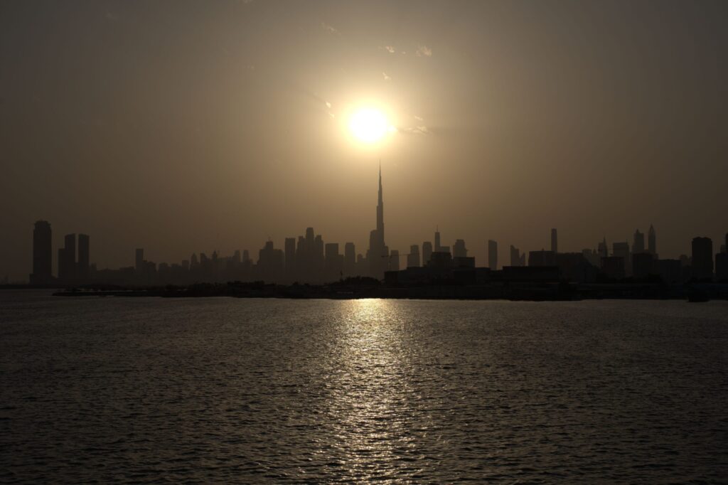 Sun setting behind the Dubai skyline over dark water