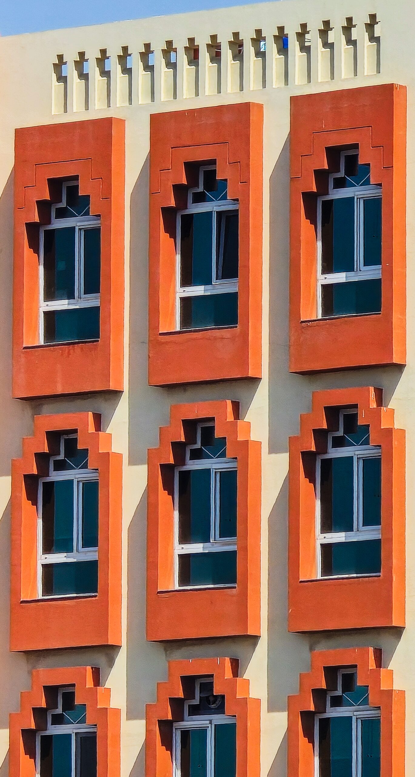 Close-up of a modern Dubai apartment building facade with geometric orange and cream window frames, representative of Binghatti East in DubaiLand Residence Complex, Dubai
