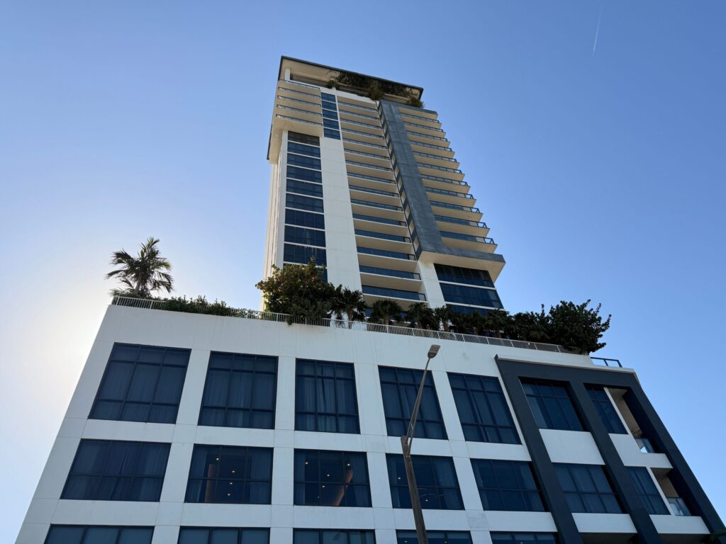 Low-angle view of a modern Dubai high-rise residential tower with white and dark-glass facade under a clear blue sky, representative of Al Sondos Lilac in DubaiLand Residence Complex, Dubai