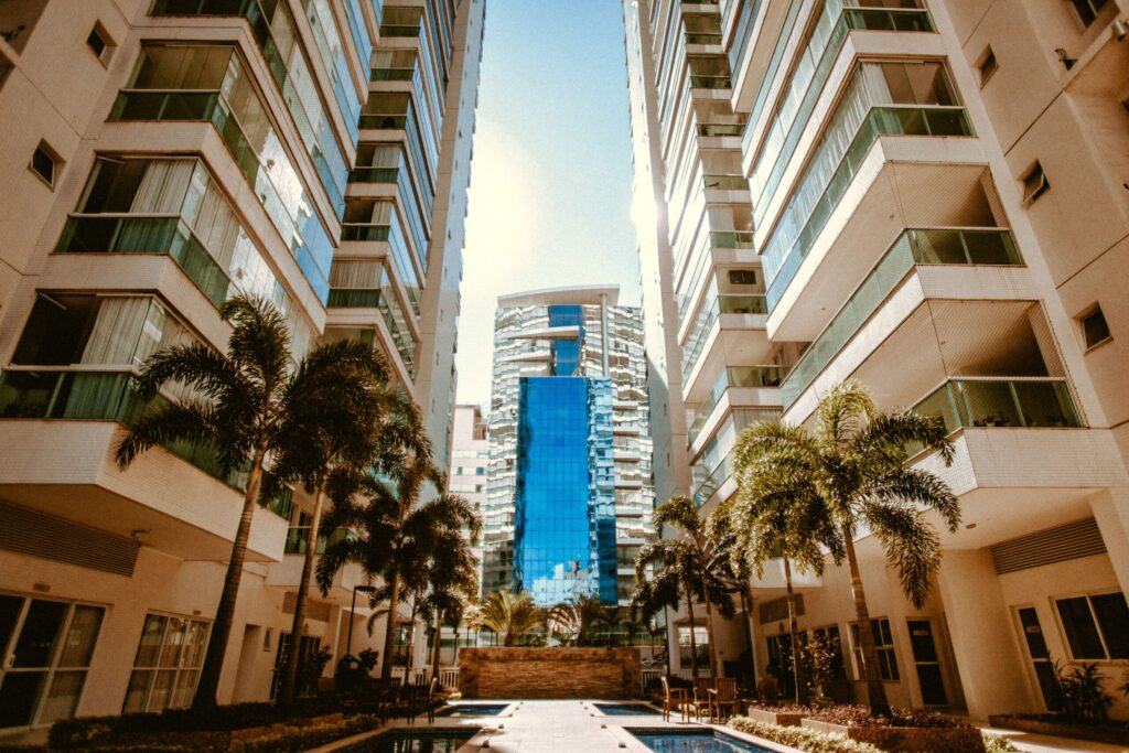 Residential towers with balconies rising between palm trees under a clear sky