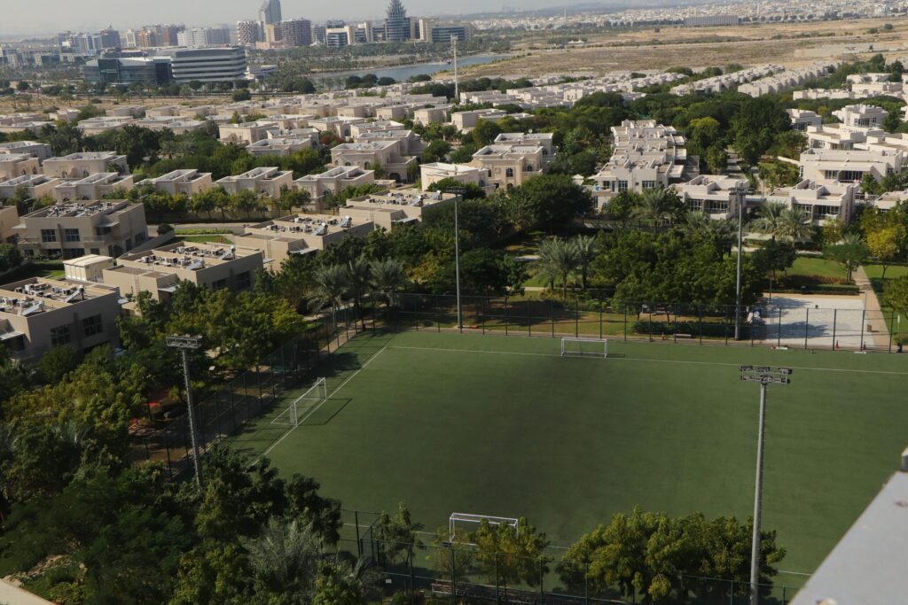 Aerial view of a gated Dubai villa community with a park and sports field near Alvorada, Arabian Ranches