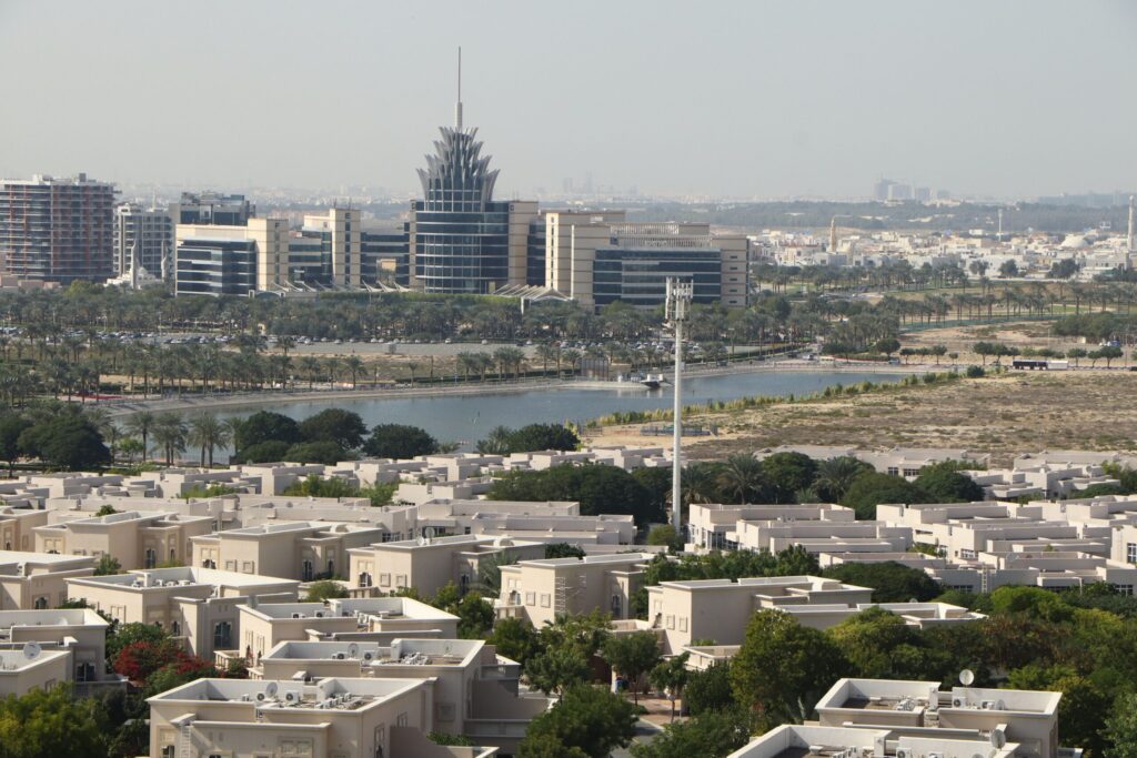 Aerial view of low-rise villa and townhouse rooftops with the Dubai skyline in the distance, near Indigo Ville 5, JVC