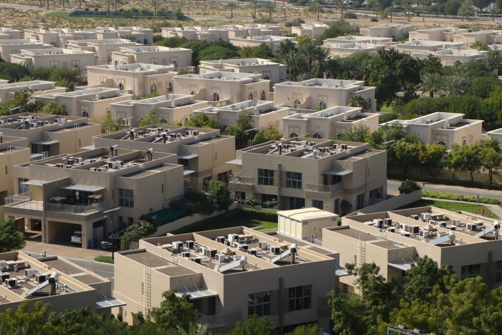Aerial view of a low-rise Dubai villa community with beige rooftops, private gardens and palm trees, representative of Majestic Vistas' gated villa setting in Dubai Hills Estate