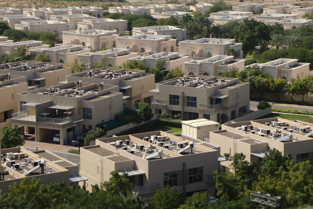 Aerial view of a low-rise Dubai townhouse community with beige rooftops, private gardens and mature trees, representative of Maple's gated townhouse clusters in Dubai Hills Estate