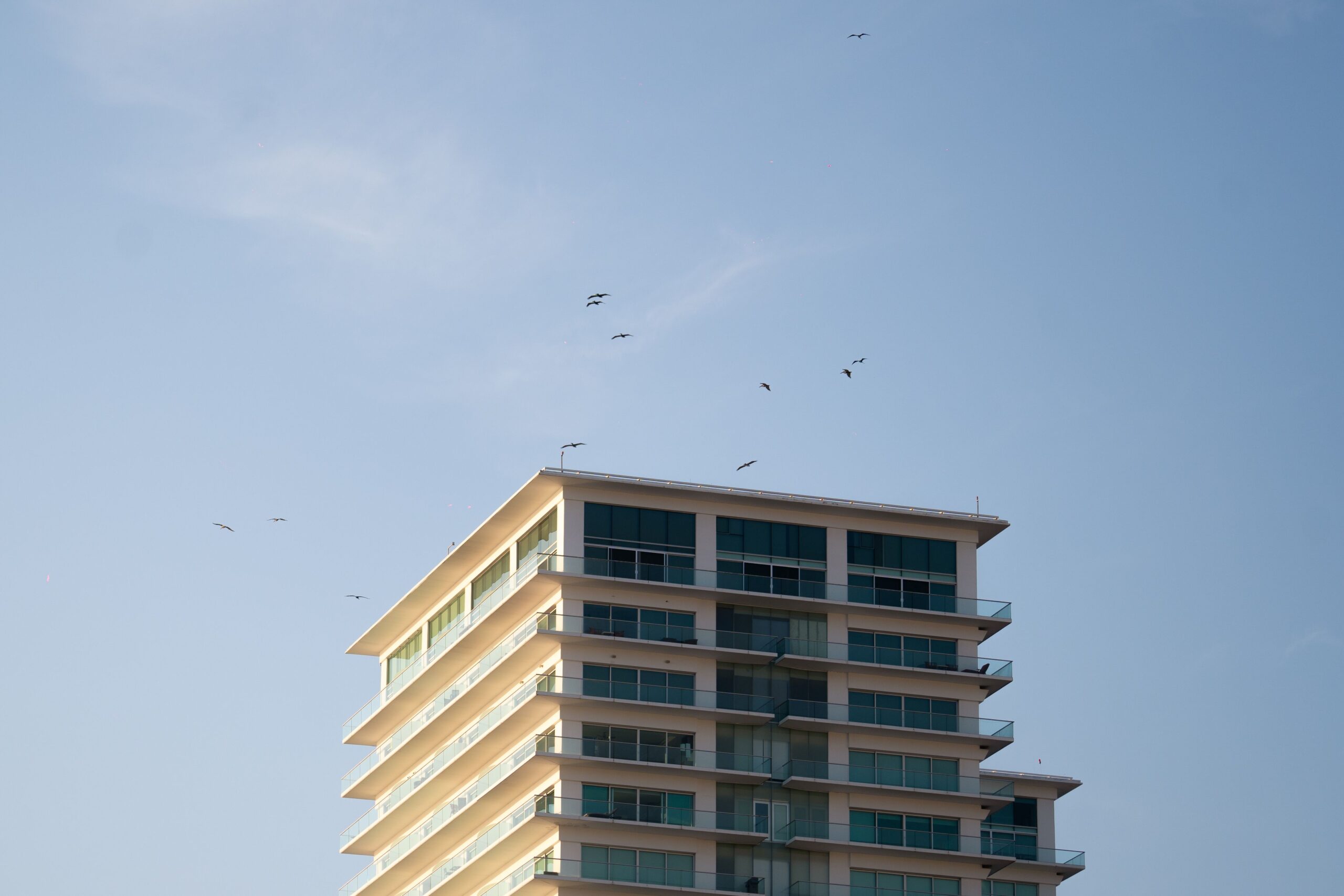 Corner view of a contemporary Dubai apartment building with glass balconies against a clear blue sky, representative of Confident Lancaster in Liwan
