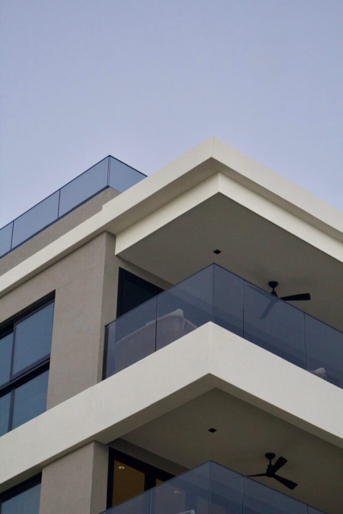 Corner view of a cream and beige modern mid-rise apartment building with glass balcony railings at dusk, representative of Executive Residences in Dubai Hills Estate