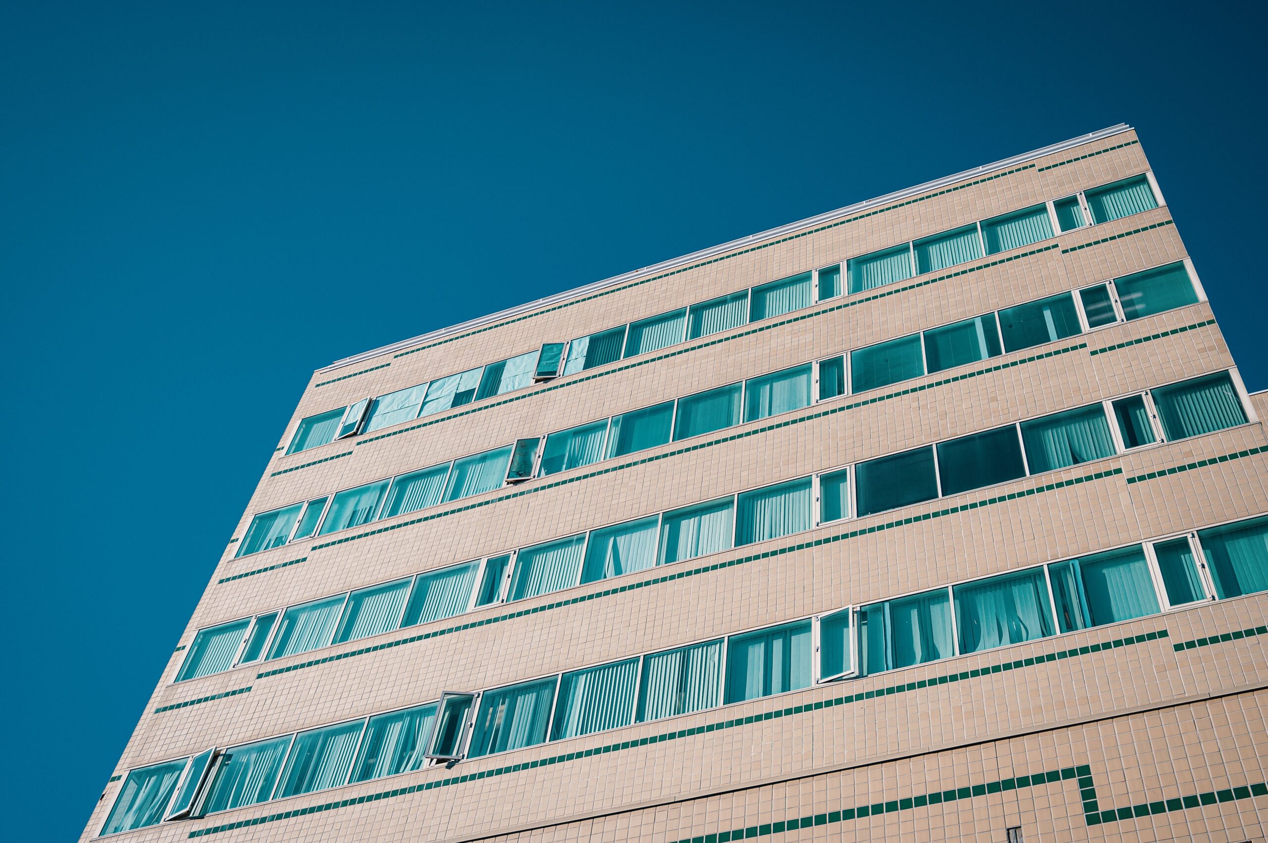 Low angle view of a tan-tiled modern apartment building with teal window trim against a deep blue sky