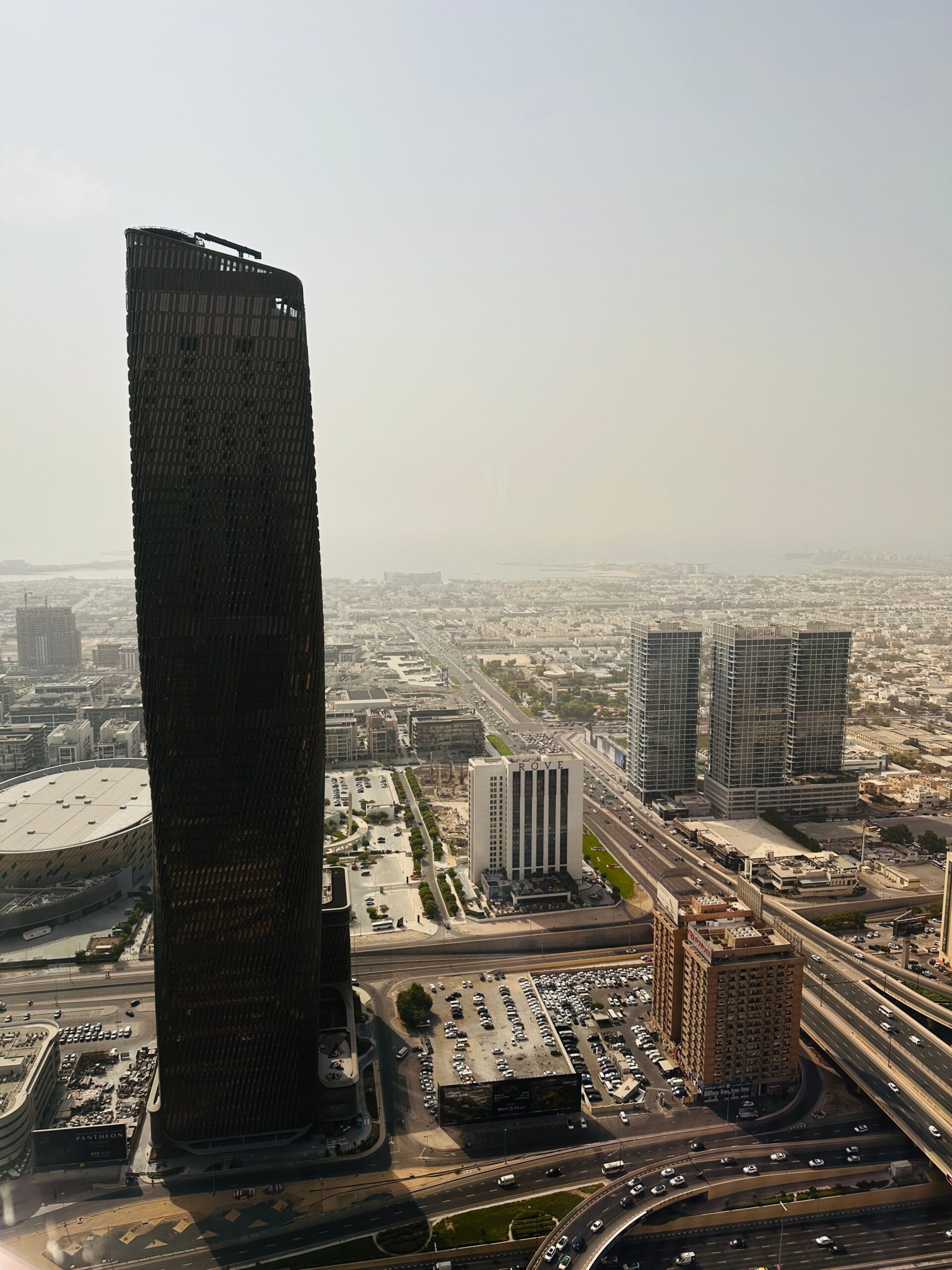 Aerial view of a dark twisted supertall tower rising above the Dubai skyline