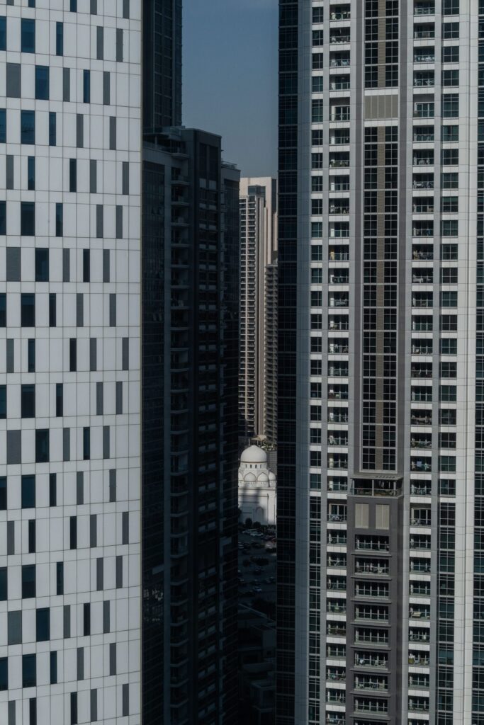 Tall glass residential towers in Dubai with a distant mosque dome visible between them, representative of the Arjan area around Divine Residences by Takmeel