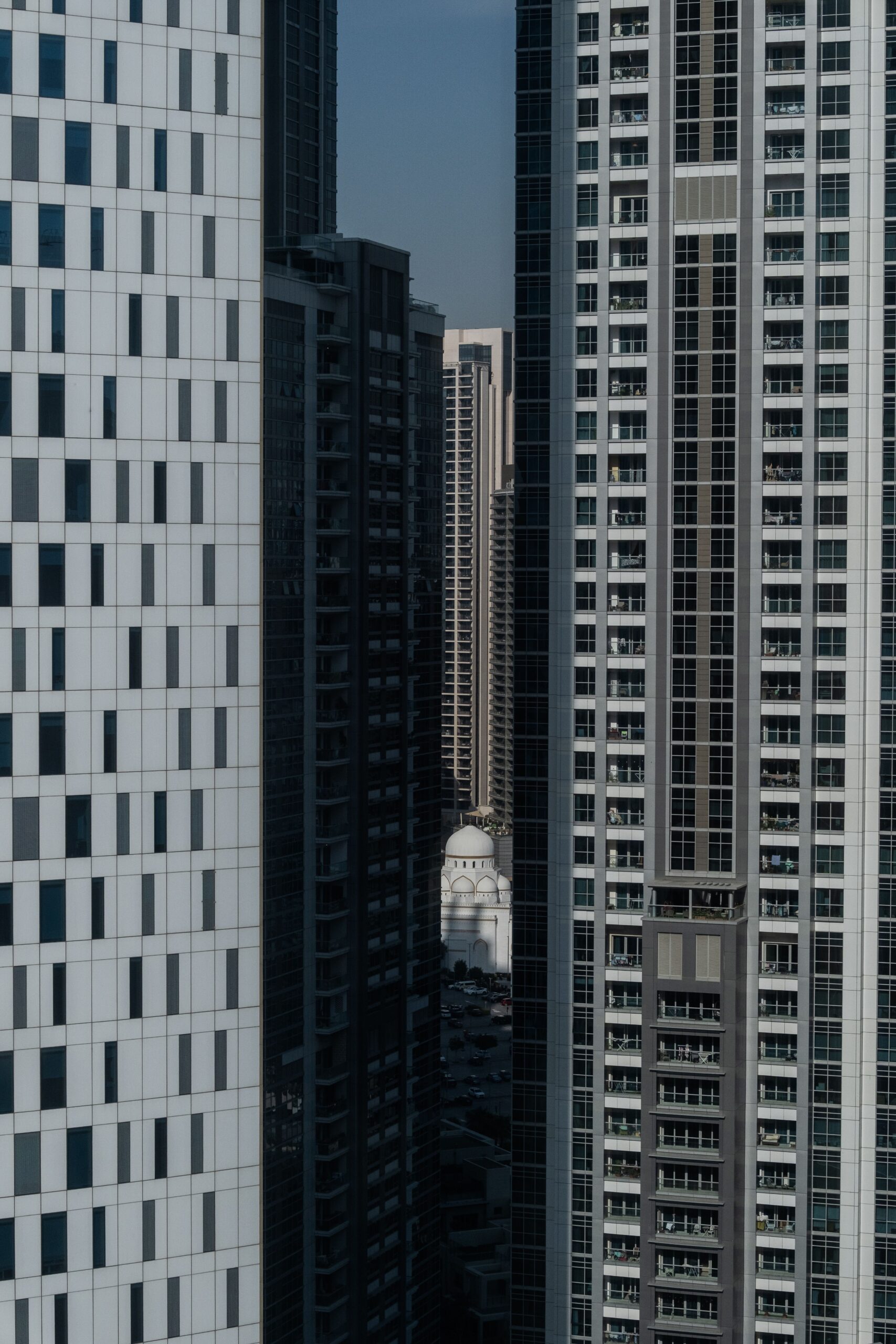Tall glass residential towers in Dubai with a distant mosque dome visible between them, representative of the Arjan area around Divine Residences by Takmeel