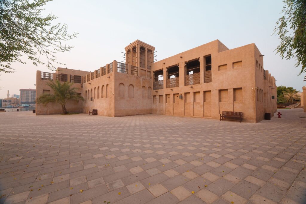 Sandstone-toned Old Town-style low-rise Arabian building with a traditional wind tower and palm tree under a clear sky in Downtown Dubai, near Miska 4