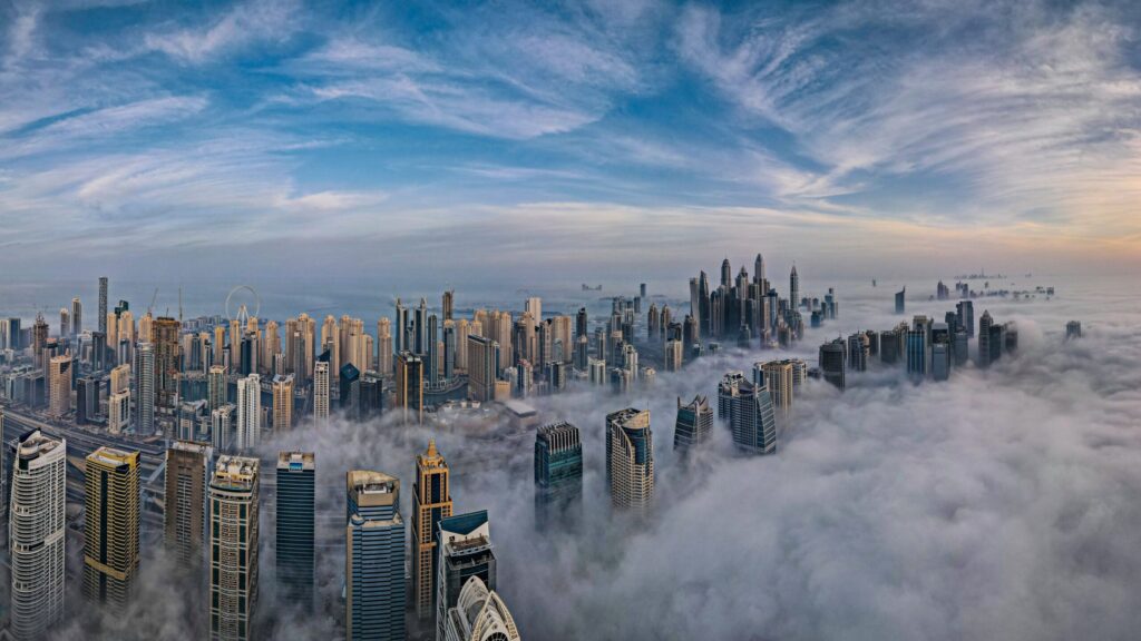 Aerial view of Dubai skyscrapers above morning fog under a blue sky