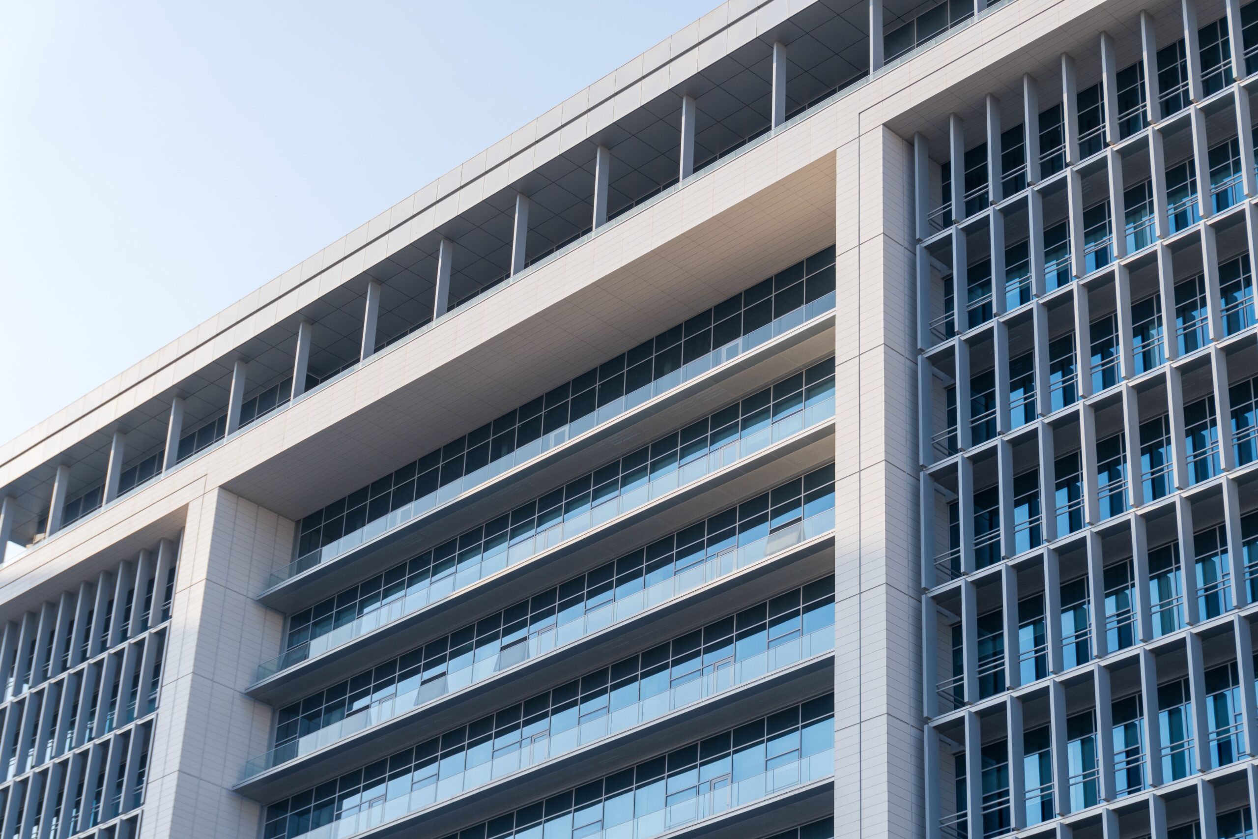 Corner view of a modern glass and concrete apartment building facade against a clear sky, Dubai