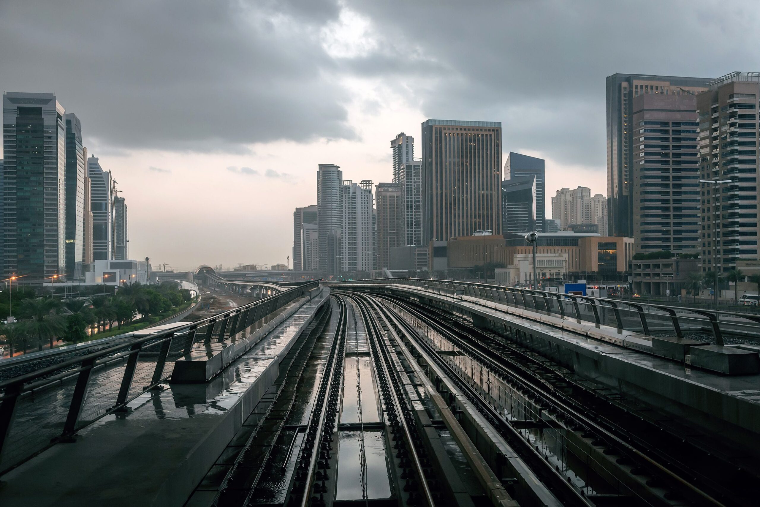 Moody, rainy-day view of a Dubai high-rise skyline seen past elevated metro tracks, representative of the JLT district near MBL Royal and its DMCC Metro Station connection
