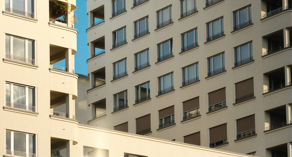 Close-up view of two adjacent cream and beige modern apartment buildings with recessed rounded balconies and grid windows under a clear sky, representative of contemporary residential architecture near Azizi Yasamine in Al Furjan, Dubai