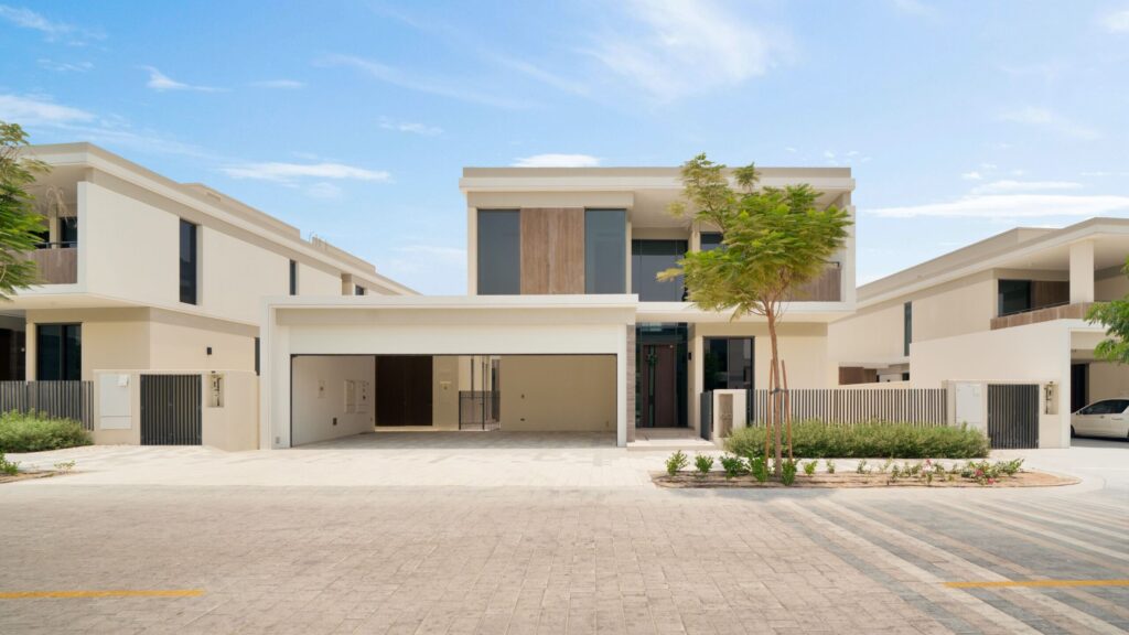 Contemporary two-story villa in a gated Dubai residential community, cream stucco facade with a driveway and integrated garage, low hedge landscaping, representative of Springs 8, The Springs, Emirates Living