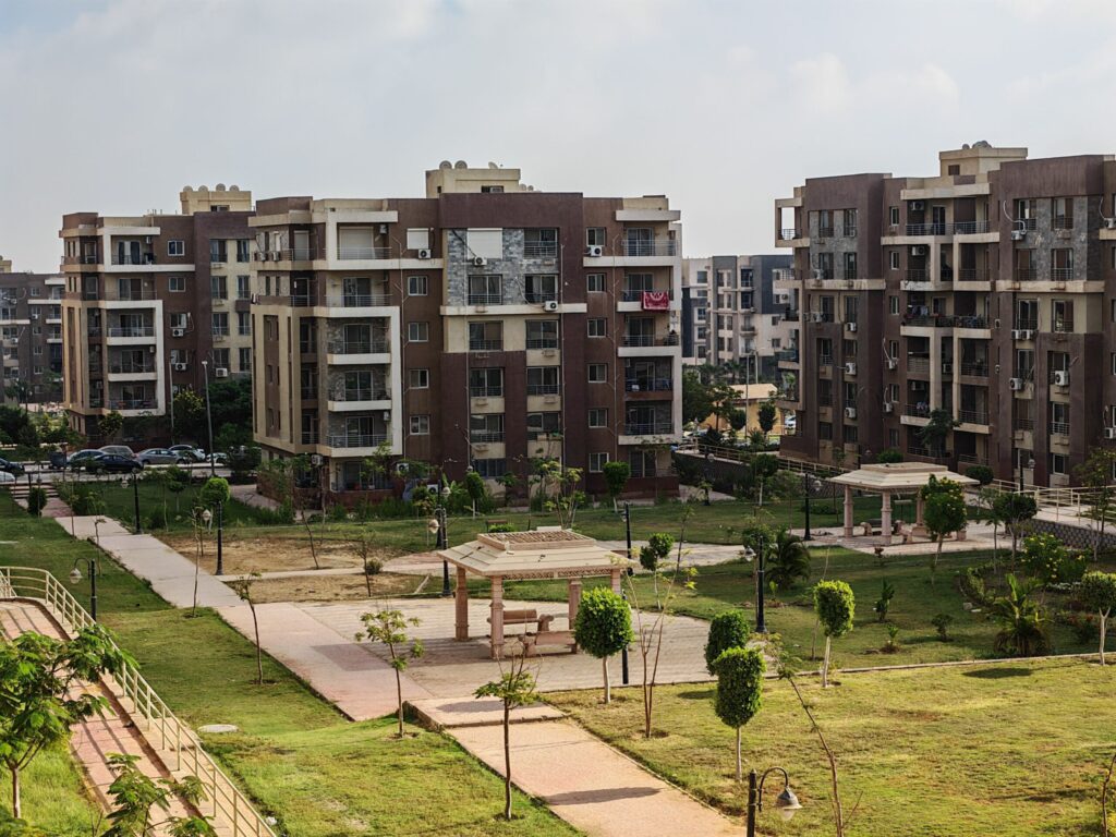 Low-rise apartment blocks around a landscaped park with pathways and a gazebo, similar in style to Green Park, JVT