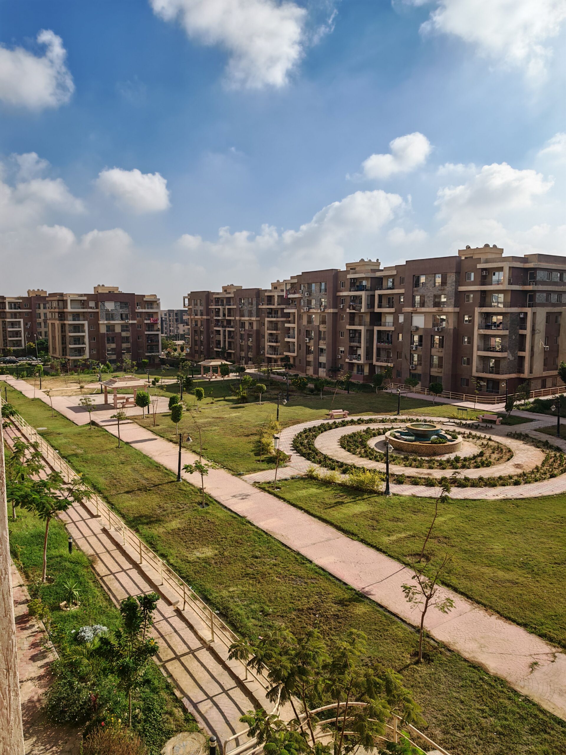 Aerial view of a mid-rise Dubai apartment complex arranged around a circular landscaped garden with a central fountain, representative of Lawnz by Danube's shared courtyard setting in International City