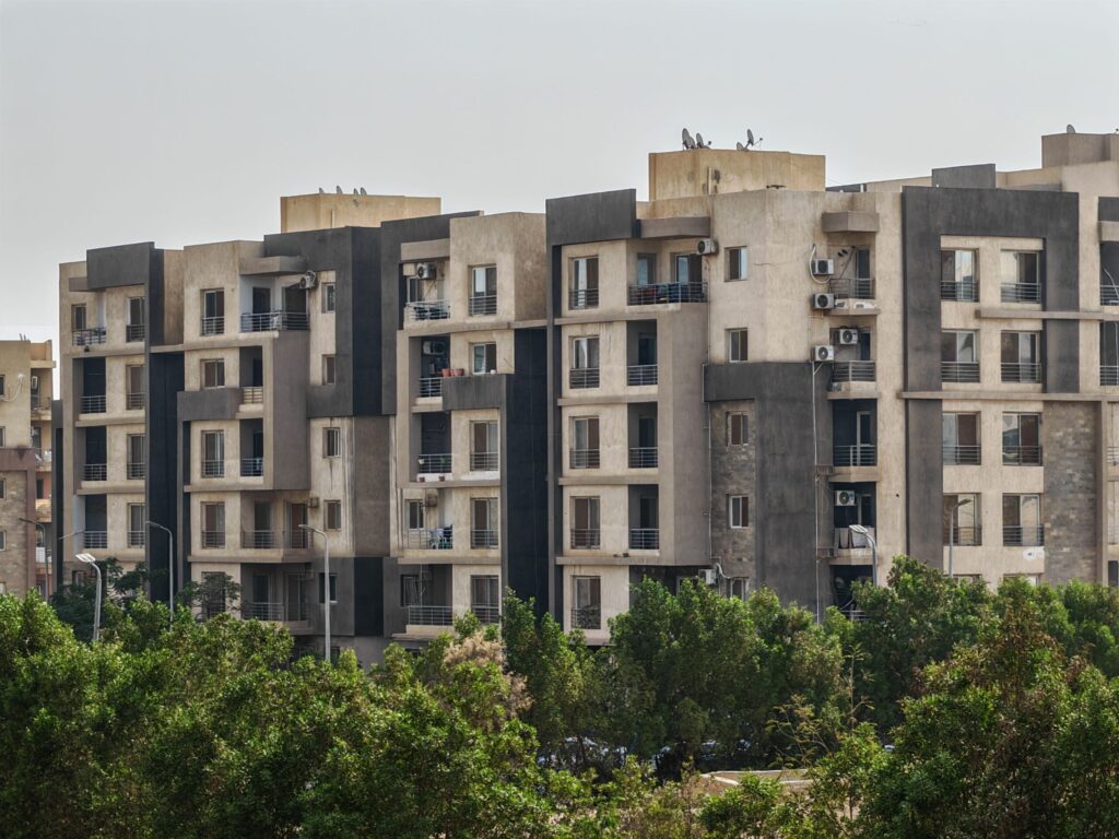 Sunlit mid-rise residential apartment complex with trees in foreground in Dubai