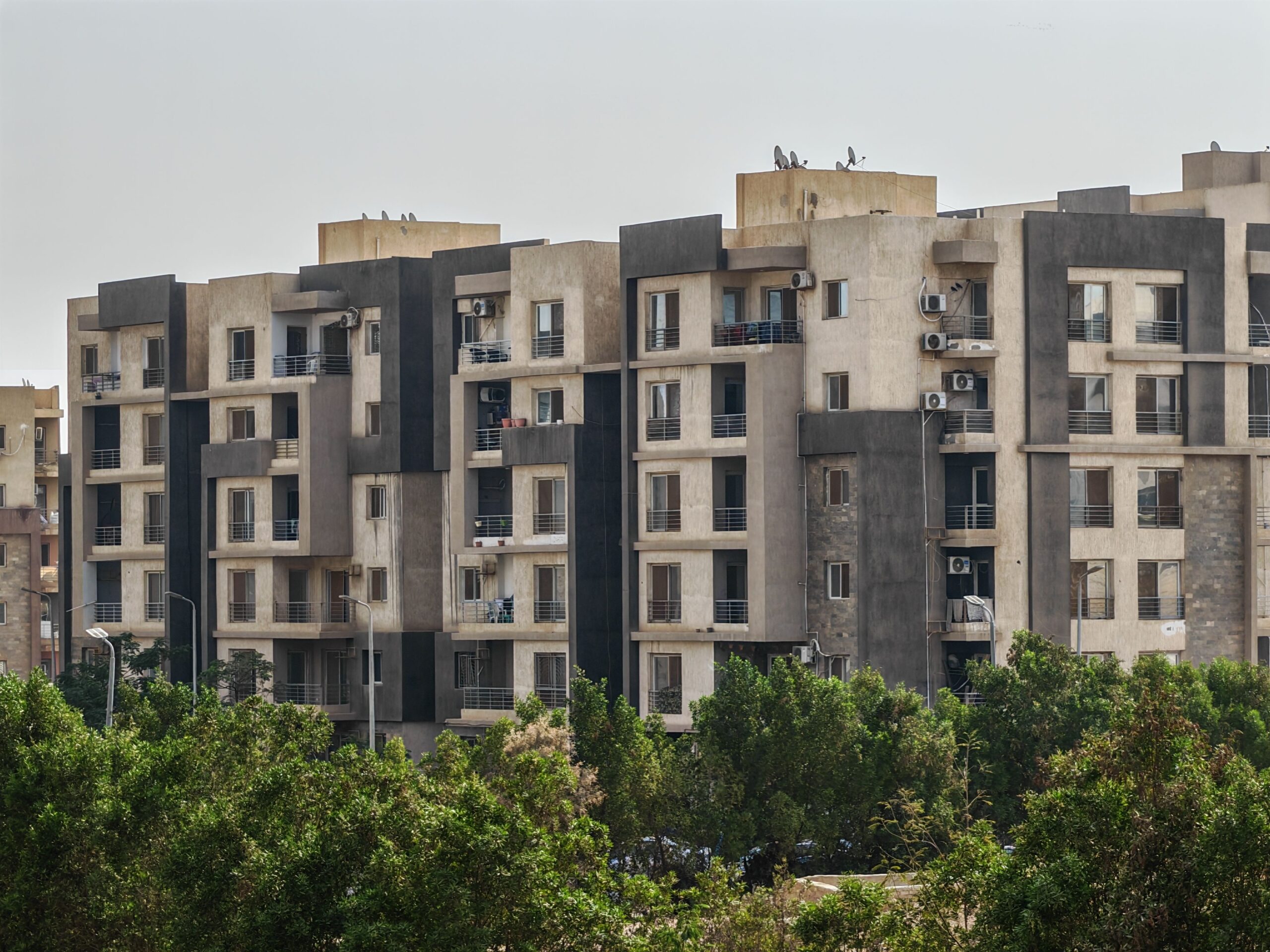Sunlit mid-rise residential apartment complex with trees in foreground in Dubai