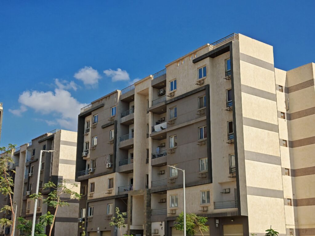 Beige mid-rise apartment building with balconies and air-conditioning units under a clear blue sky in Dubai, representative of Azizi Shaista's residential architecture in Al Furjan