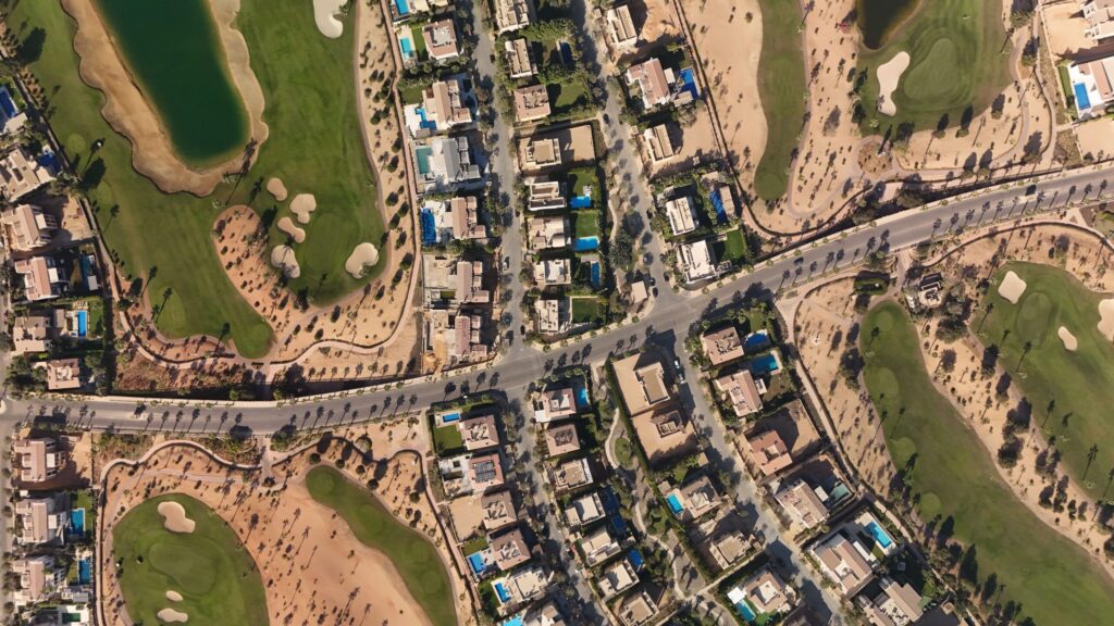 Aerial view of a golf-course villa community with individual private pools and tree-lined streets, echoing the golf-frontage villa plots of Emerald Hills, Dubai Hills Estate