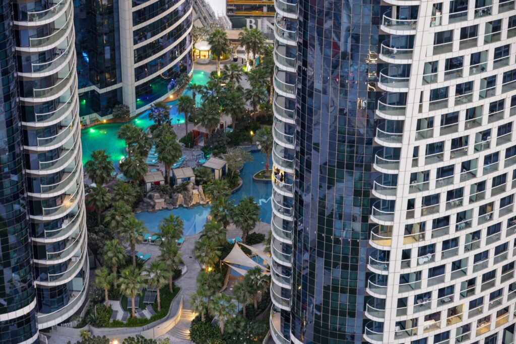 Aerial view of high-rise apartment towers around a landscaped pool deck in Dubai at dusk