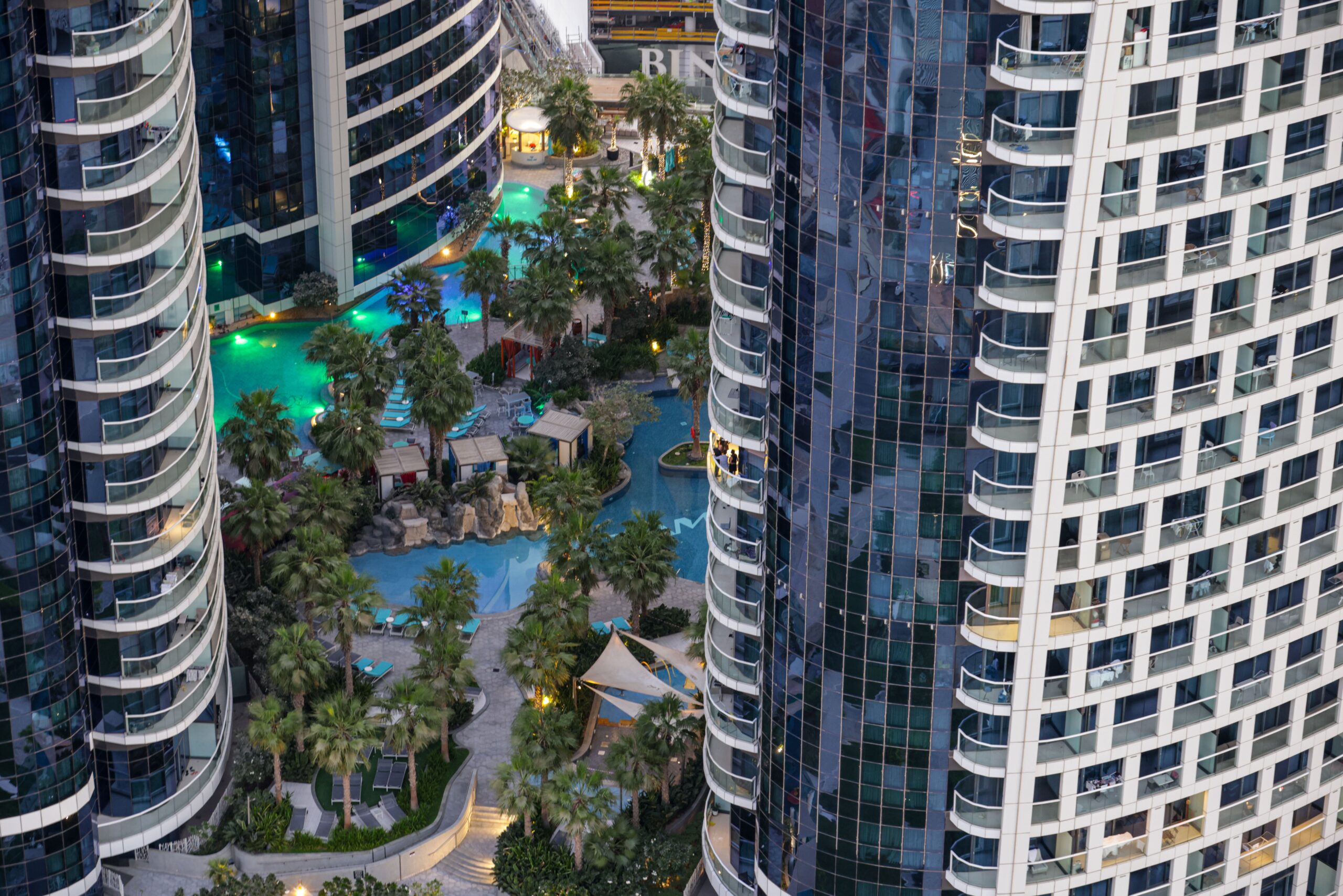 Aerial view of high-rise apartment towers around a landscaped pool deck in Dubai at dusk