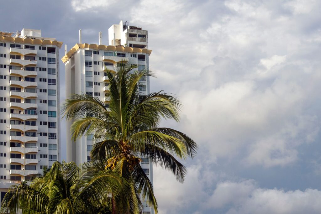 Two white residential towers beside a palm tree under a cloudy sky, near Laya Residences, Jumeirah Village Circle, Dubai