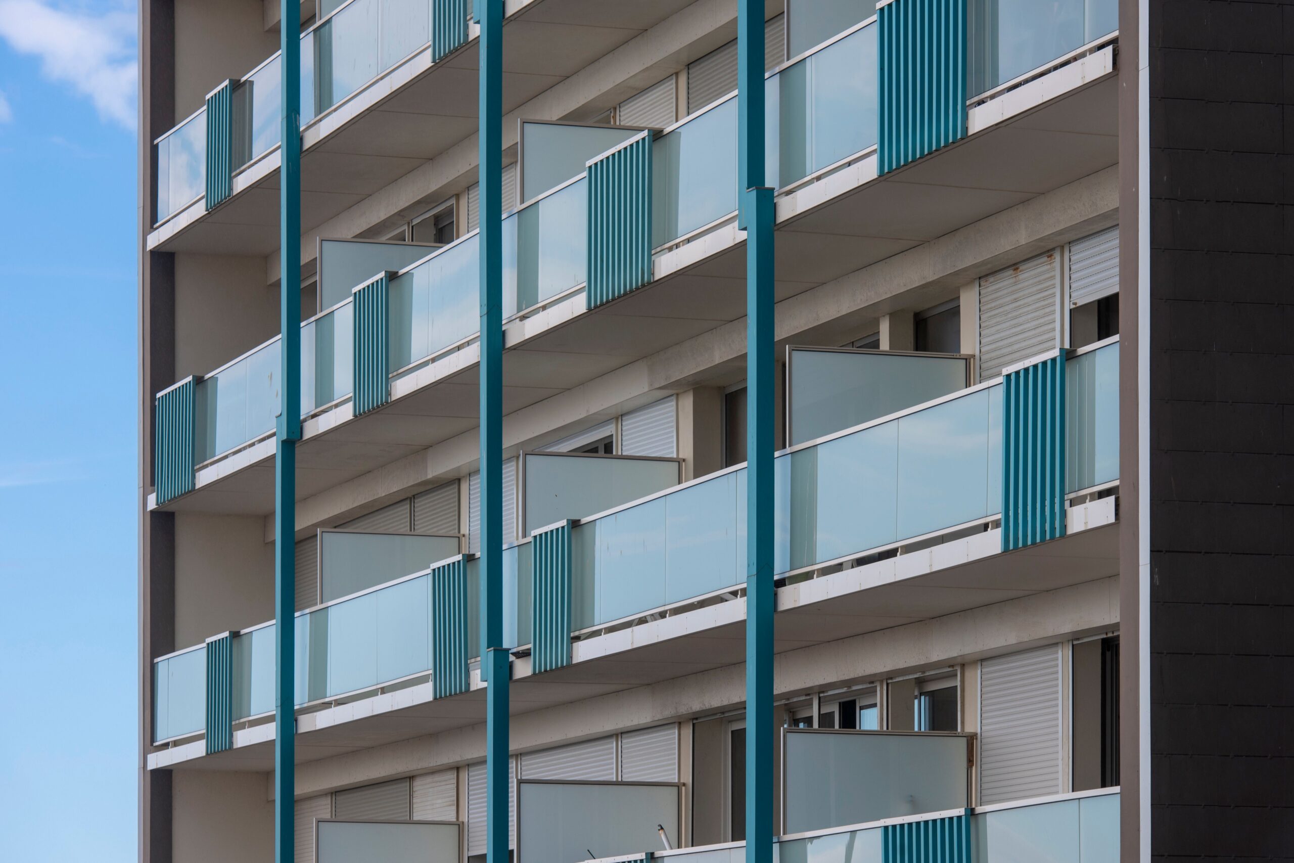 Modern apartment building with glass balcony railings and teal accents against a blue sky