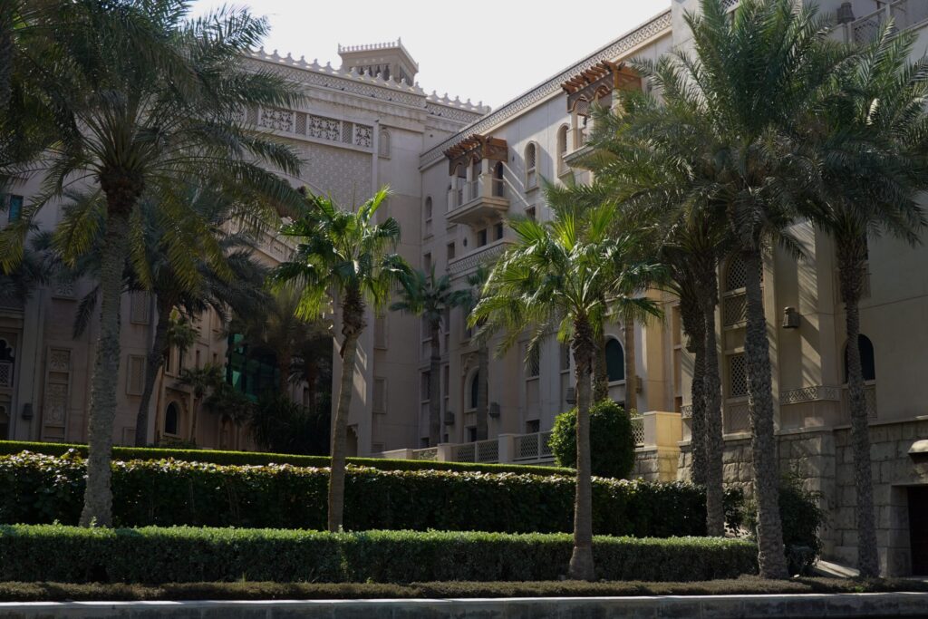 Sand-coloured mid-rise residential building with palm trees and clipped hedges under bright Dubai sunlight