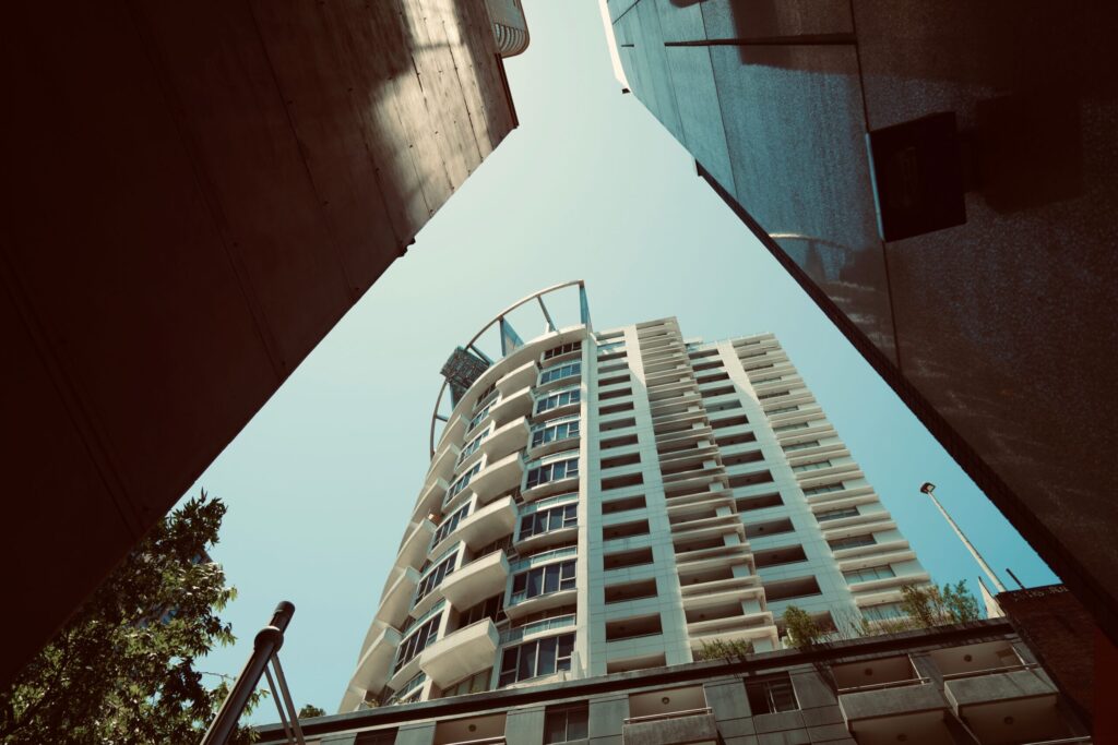 Upward view of a modern high-rise apartment tower with balconies against a clear blue sky in Dubai