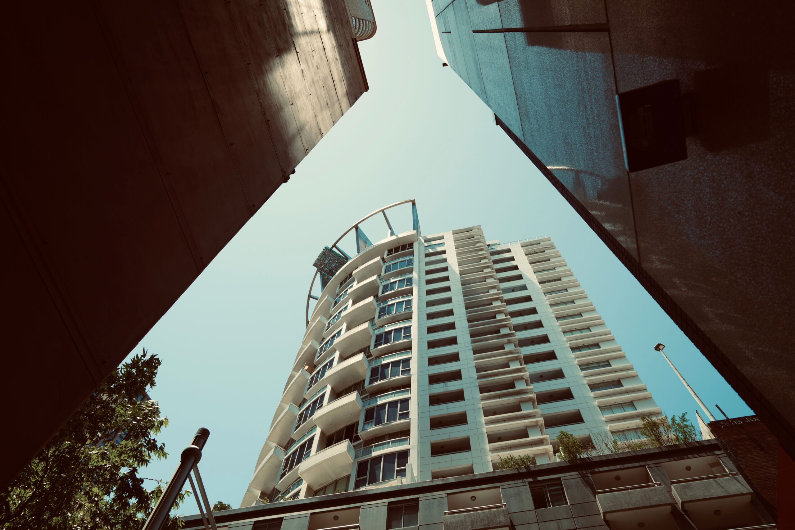 Upward view of a modern high-rise apartment tower with balconies against a clear blue sky in Dubai