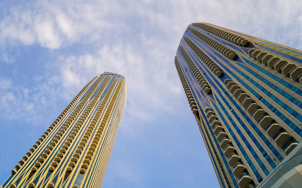Two modern high-rise towers viewed from below against a clear blue sky in Dubai