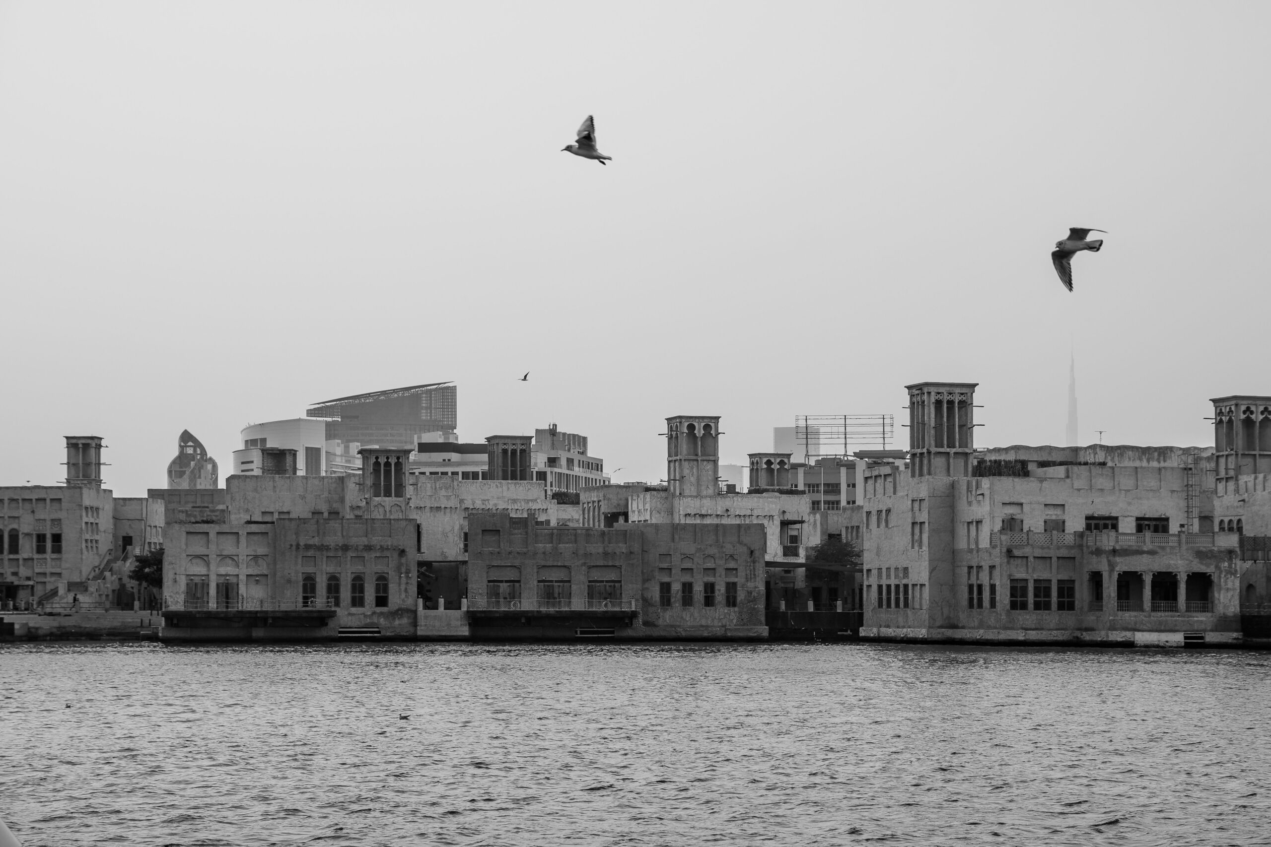 Black and white view of Dubai Creek wind-tower skyline with birds in flight, near Miska 5, Old Town, Downtown Dubai