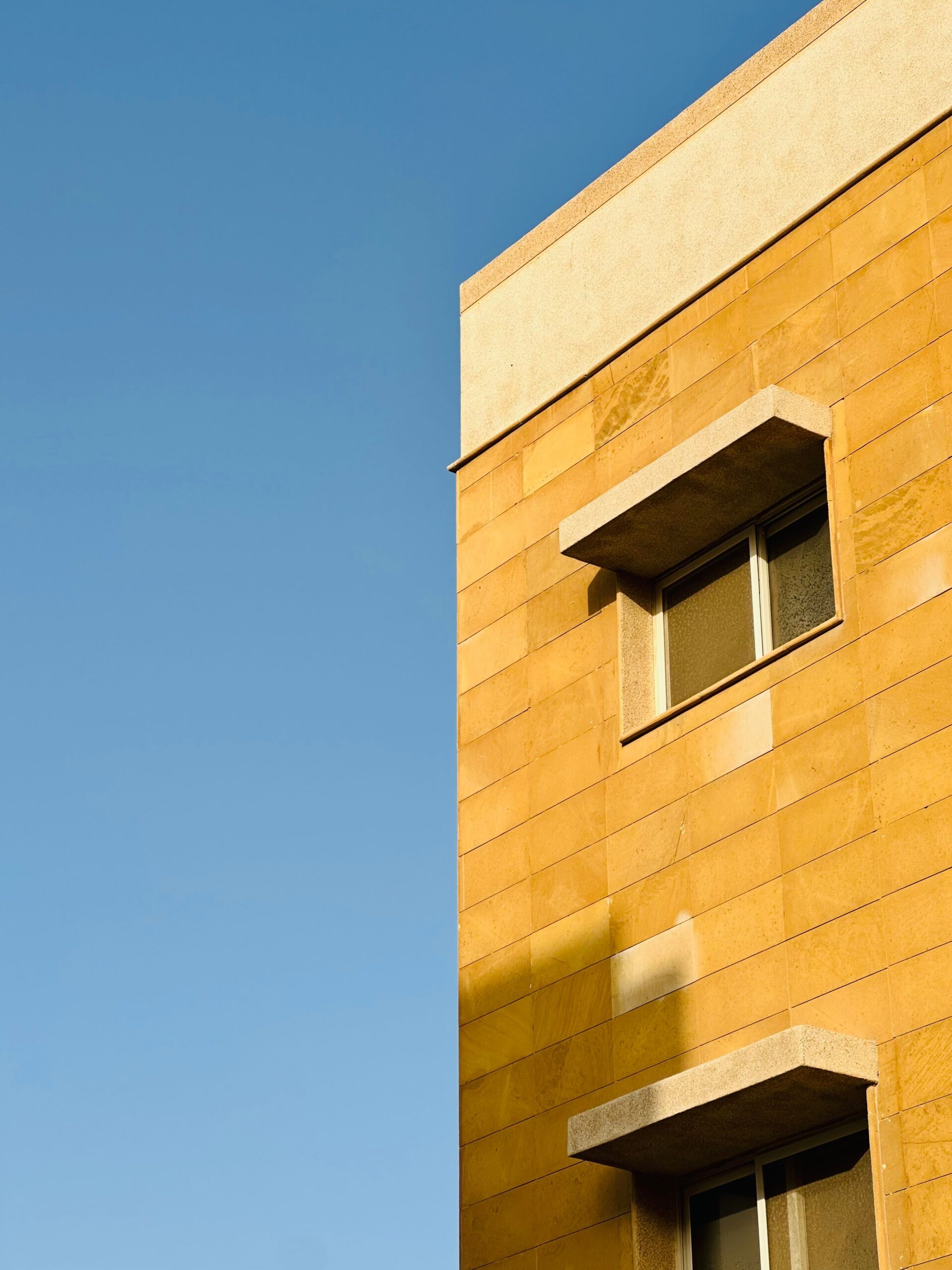 Sandstone-toned apartment building corner with a single window against a clear blue sky in Dubai