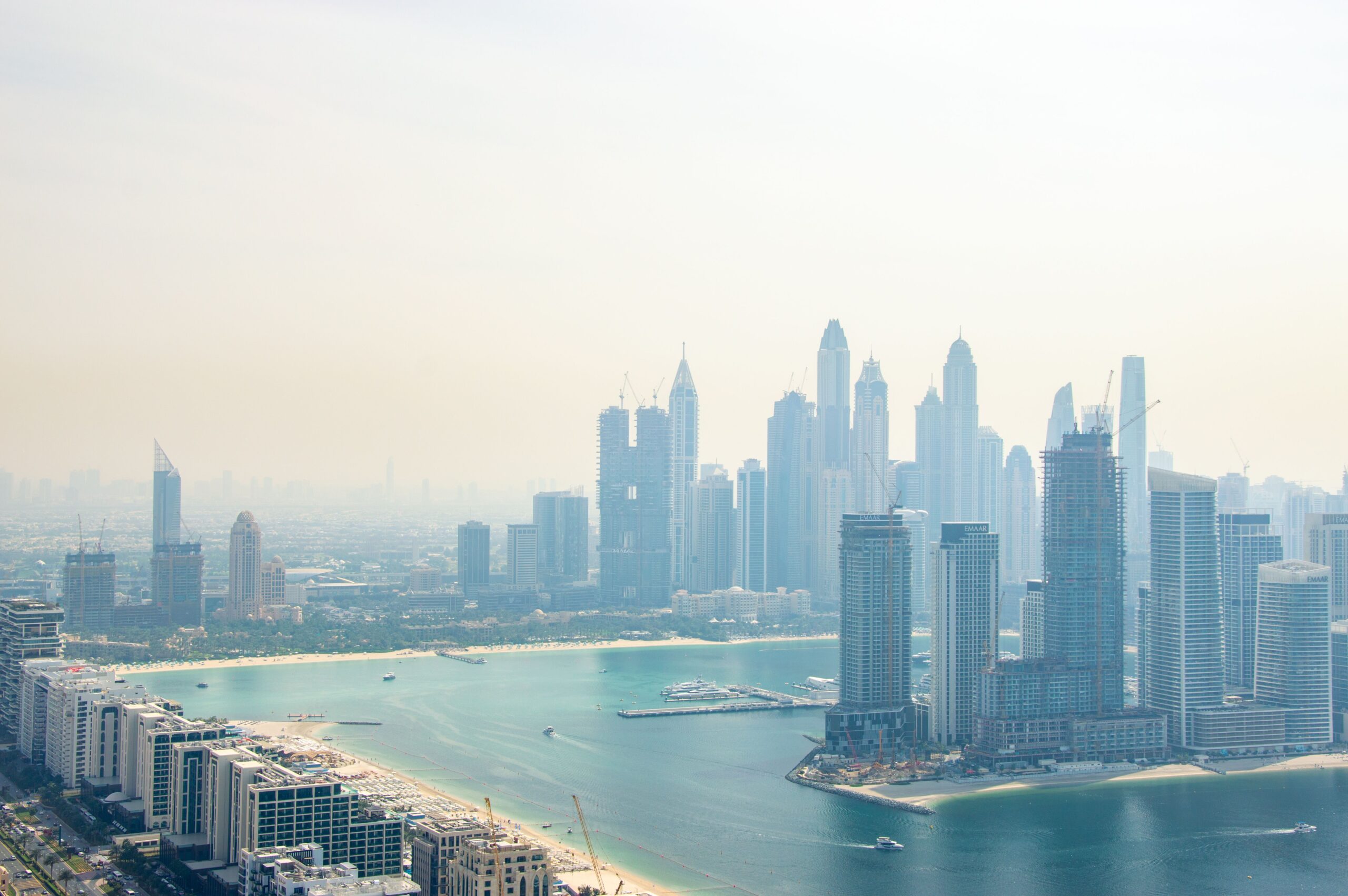 Hazy daytime aerial view of a Dubai waterfront skyline with high-rise residential towers along a lagoon-style coastline, illustrative of the Meydan waterfront setting of Azizi Riviera 69