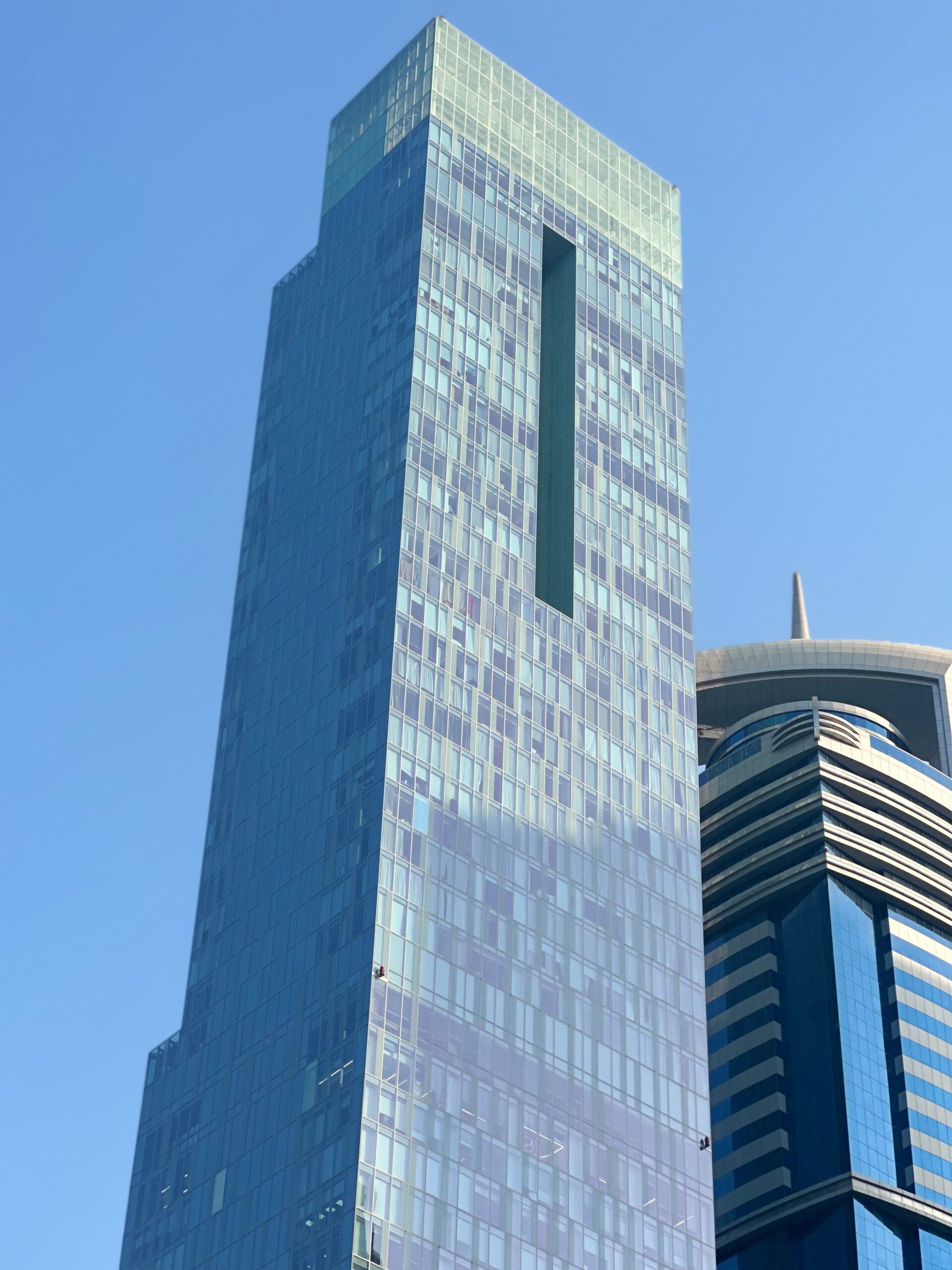 Tall modern glass residential tower reflecting light against a clear blue sky, representative of high-rise buildings near Miraclz by Danube in Arjan, Dubai