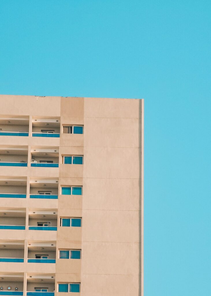 Clean modern apartment building facade with glass balconies under a clear blue sky, similar in style to The Residence by Prestige One, JVC