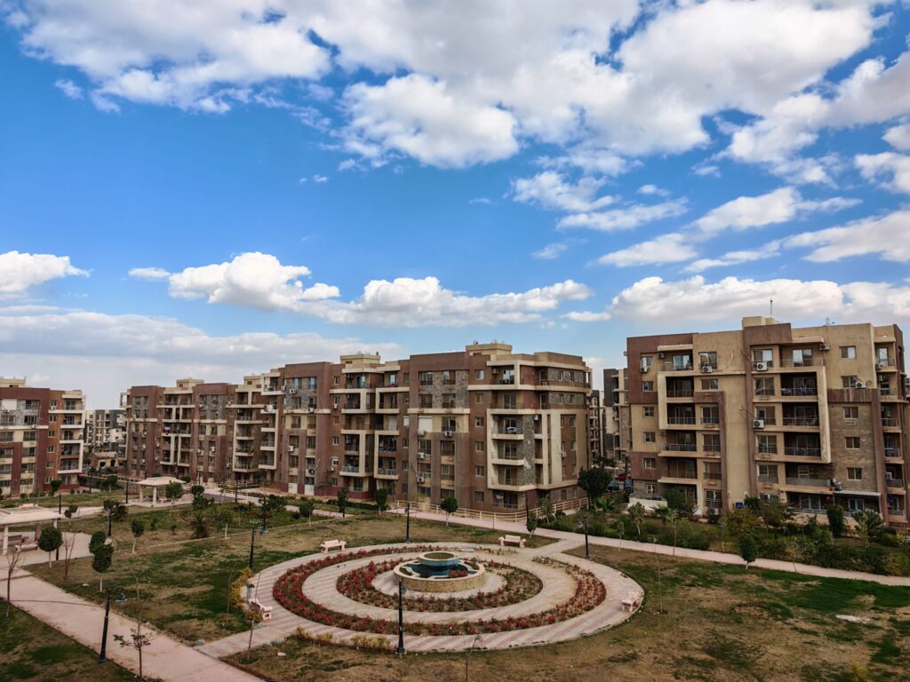 Aerial daytime view of a mid-rise Dubai apartment complex with a landscaped garden and central fountain